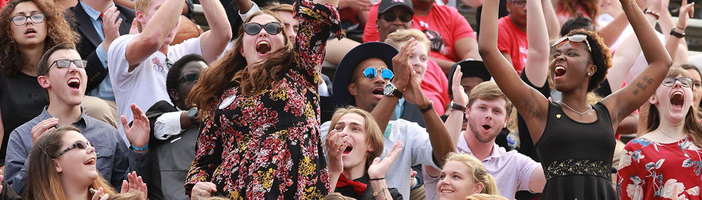 Many cheering faces in stadium seating. three rows and ten across.